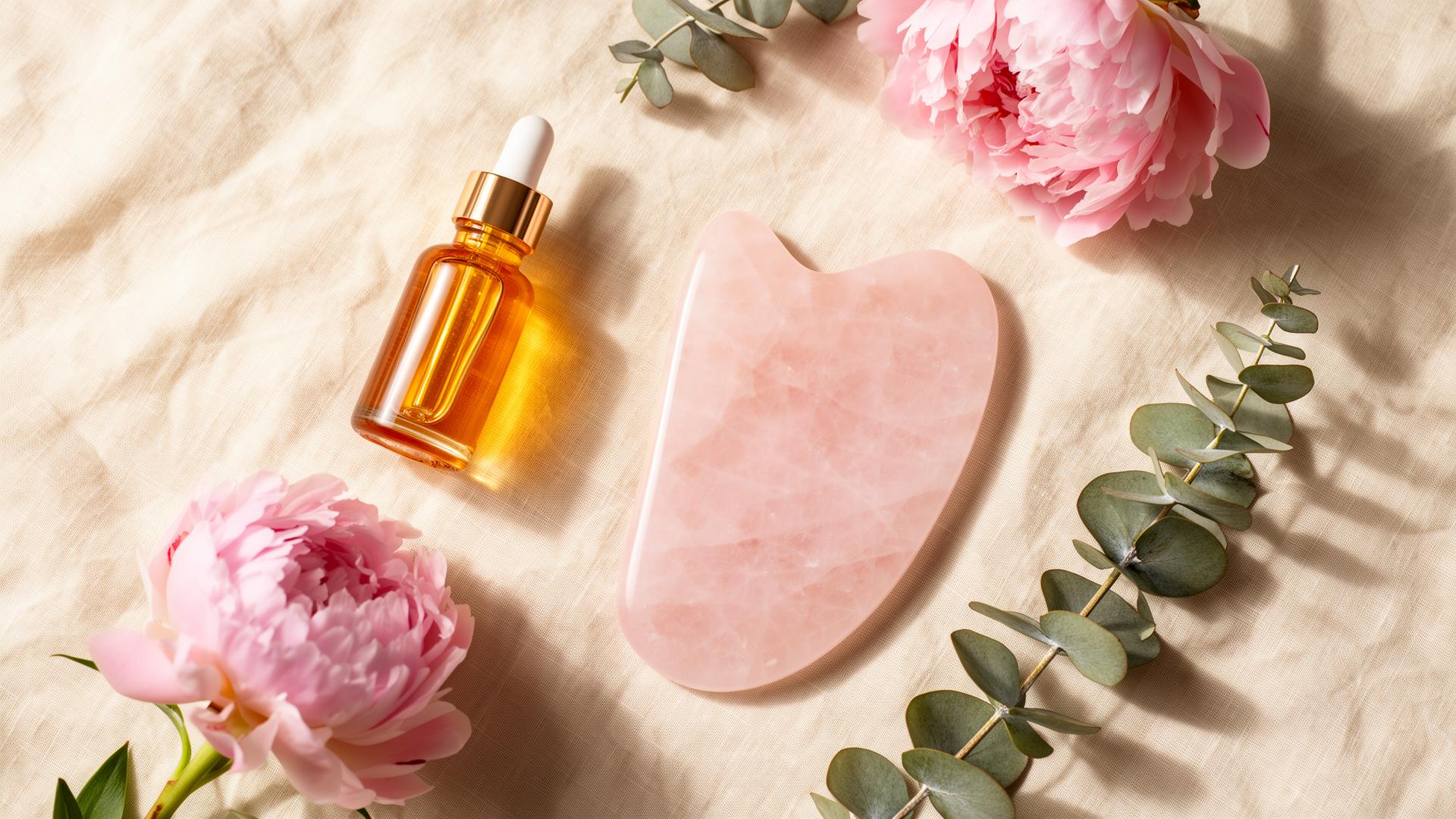 Luxury spa flatlay with amber serum, rose quartz gua sha stone, peonies and eucalyptus
